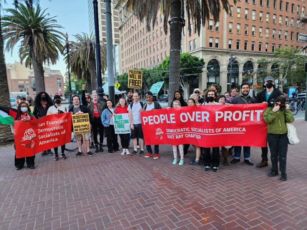 A photo of DSA SF and East Bay DSA members posing for a group photo. People are holding pro-Palestinian liberation signs, as well as a DSA SF and East Bay DSA banner.