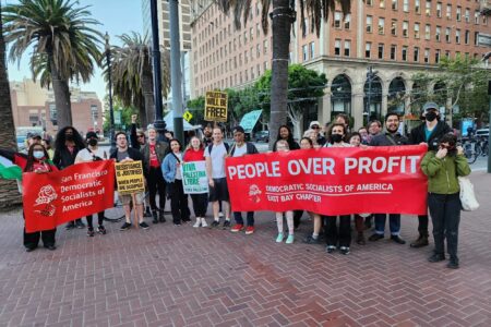 A photo of DSA SF and East Bay DSA members posing for a group photo. People are holding pro-Palestinian liberation signs, as well as a DSA SF and East Bay DSA banner.