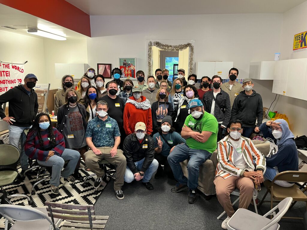 A group of more than 30 people sitting in DSA SF's office and posing together for a group photo. Everyone is wearing masks.