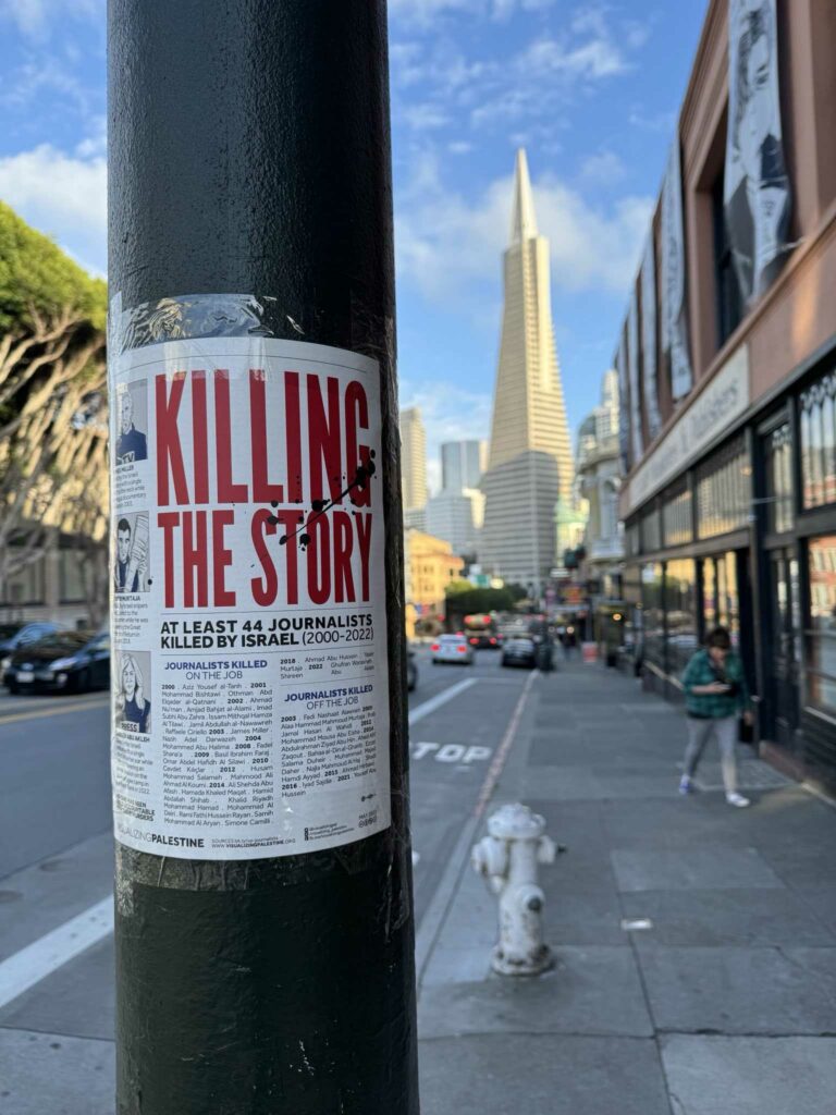 A poster taped to a lamp post. In bold red text, the poster reads, "KILLING THE STORY: At least 44 journalists killed by Israel (2000-2022)." The poster includes additional details that are too small to read in the photo. The Visualizing Palestine logo is visible at the bottom of the poster.