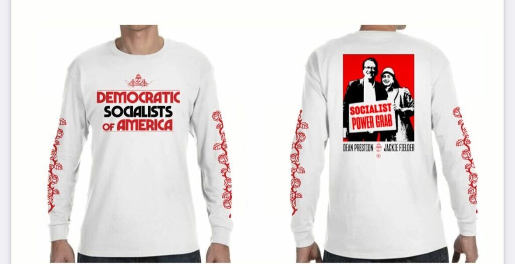 A photo showing a white long-sleeved t-shirt design from the front and the back. The front of the t-shirt has the DSA SF logo above red and black text that says "Democratic Socialists of America." There are red rose designs going up both of the sleeves. The back of the shirt has a picture of Dean Preston and Jackie FIelder in black, red, and white with a sign that says "SOCIALIST POWER GRAB." Below the image is text that says "Dean Preston" and "Jackie Fielder" with the DSA SF logo between their names.